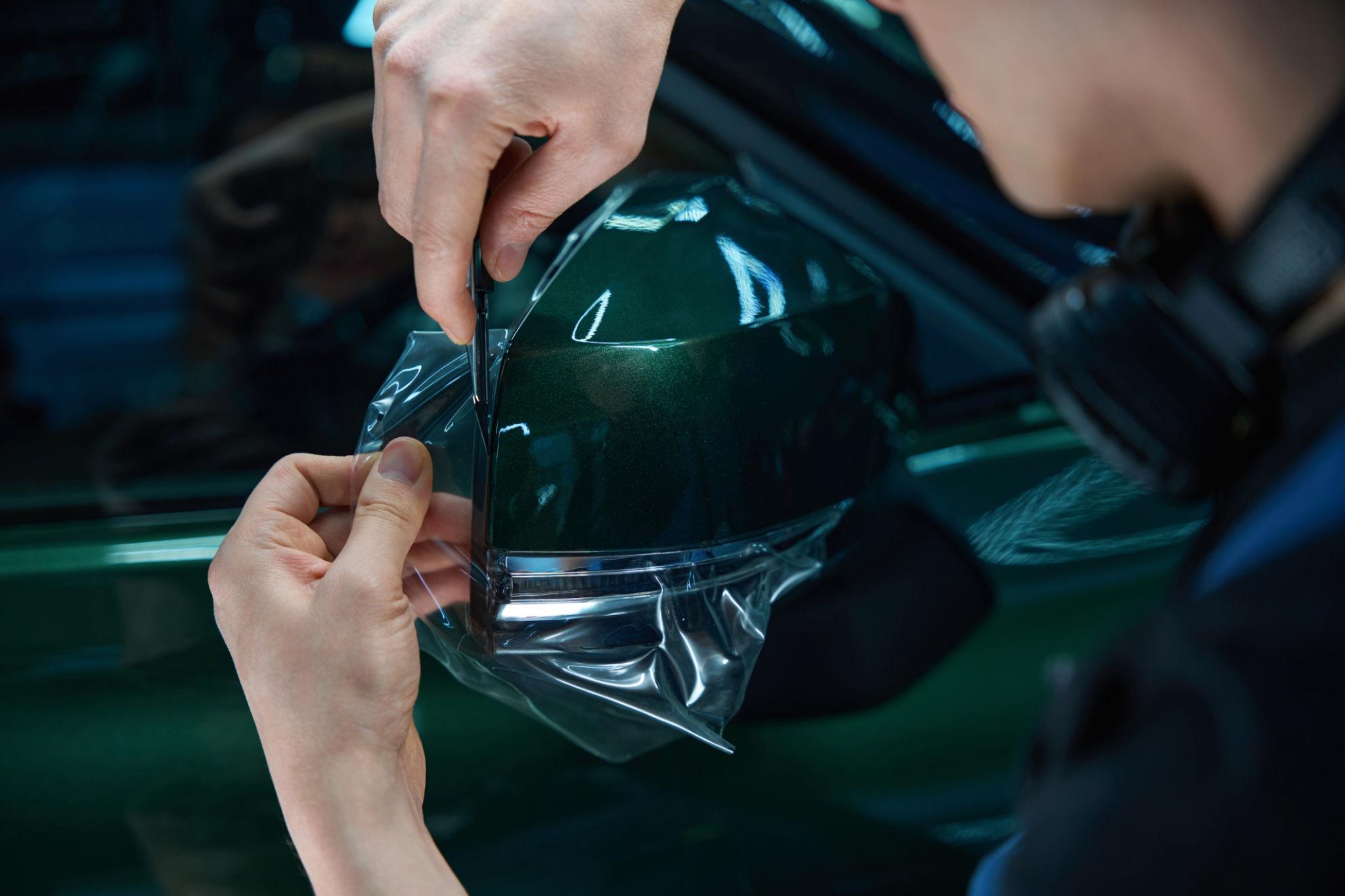 Technician applying paint protection film on car side mirror with precision cutting